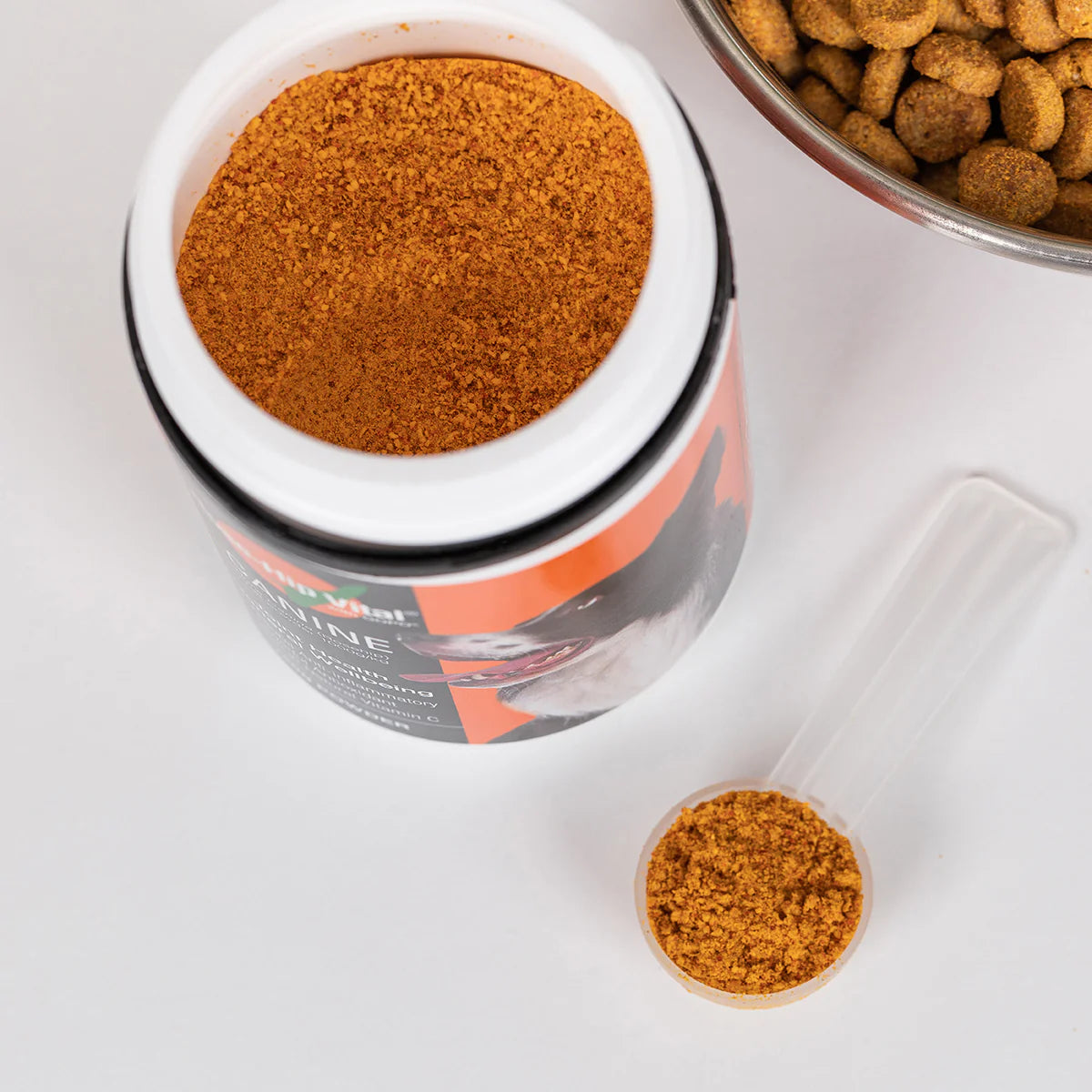 Container of Dog joint health supplement made from pure rosehip berries for pain relief and cartilage protection, spoonful of powder, and bowl of dog food on a white surface.